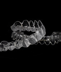 Two clear dental aligners stacked against dark background