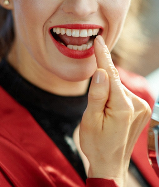 Woman smiling and pointing to dental crown in Edmonton