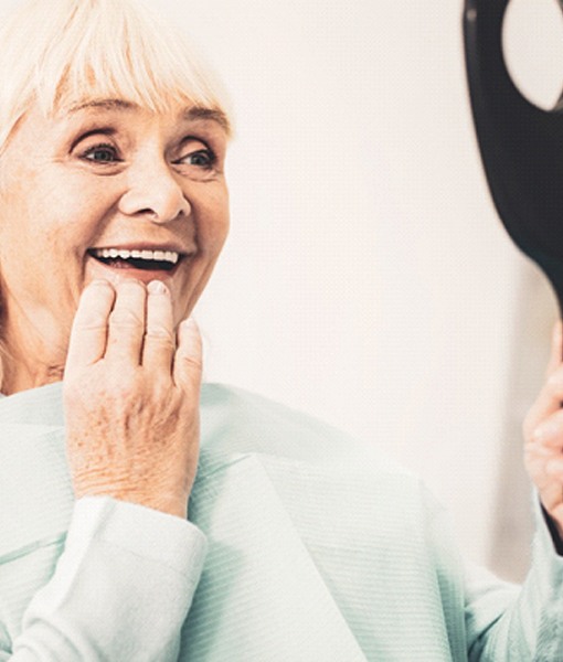 Senior dental patient holding mirror, admiring her dentures
