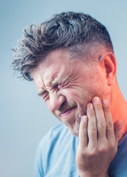 Man in need of emergency dentistry holding his cheek in pain