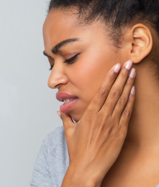 Woman in need of T M J therapy holding jaw in pain