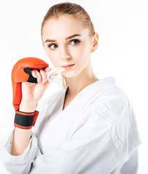 Young female athlete in white robe holding mouthguard for sports