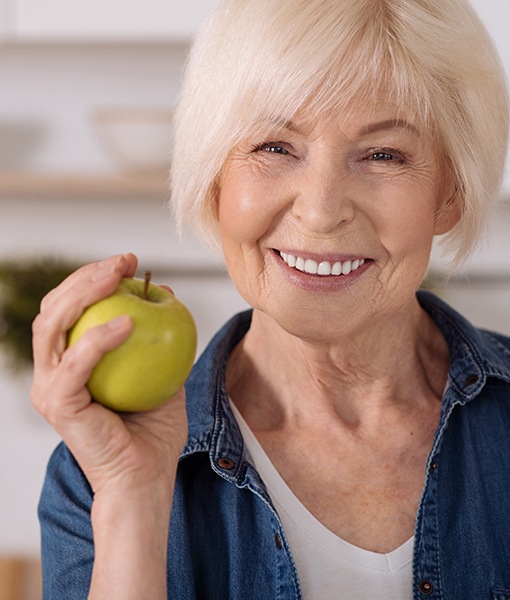 Woman with dental implant supported replacement teeth holding green apple