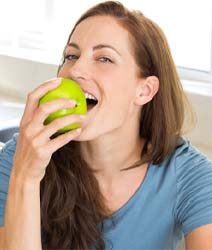 Woman with dental implants in Edmonton, Canada eating an apple