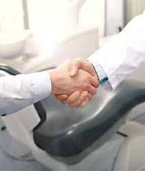 Dentist and patient shaking hands in front of chair