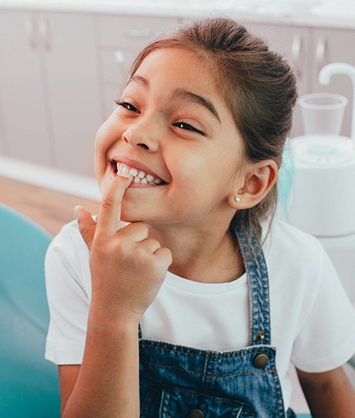 Little girl with dental sealants pointing to her smile