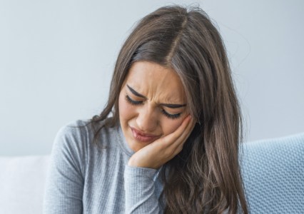 Woman in need of restorative dentistry holding cheek in pain