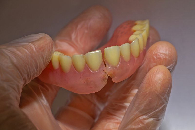 A hand holding ill-fitting dentures